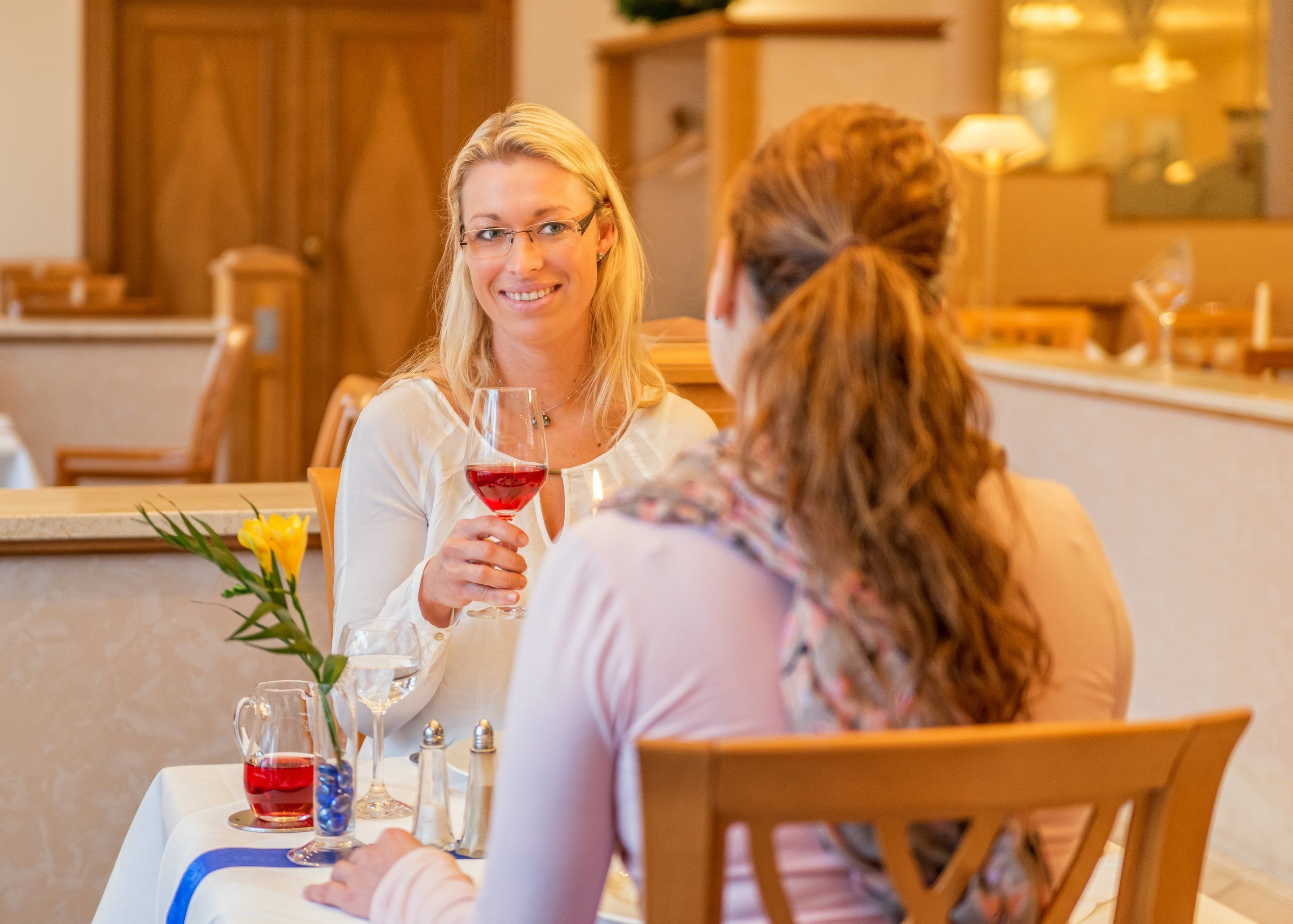 Two people seated at a table with a wine glass, a pitcher, and a vase with flowers.