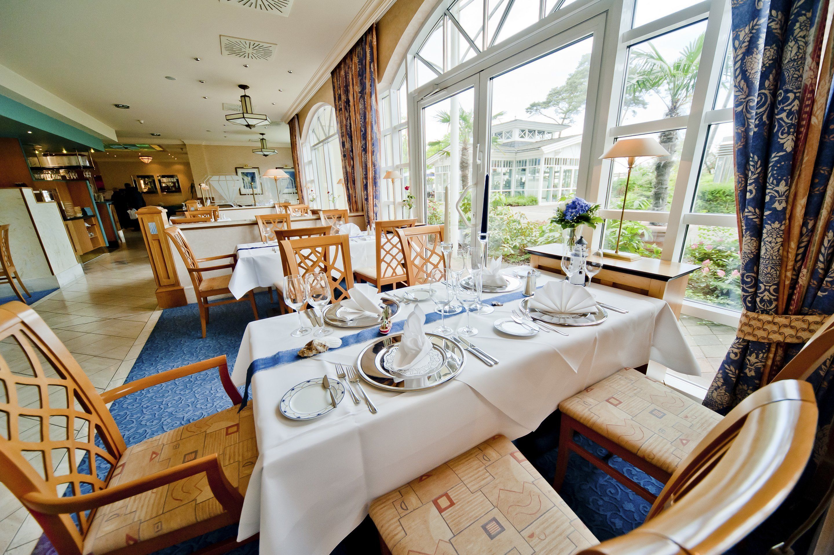 A dining area with tables set for a meal, large windows, and a view of the outdoors.