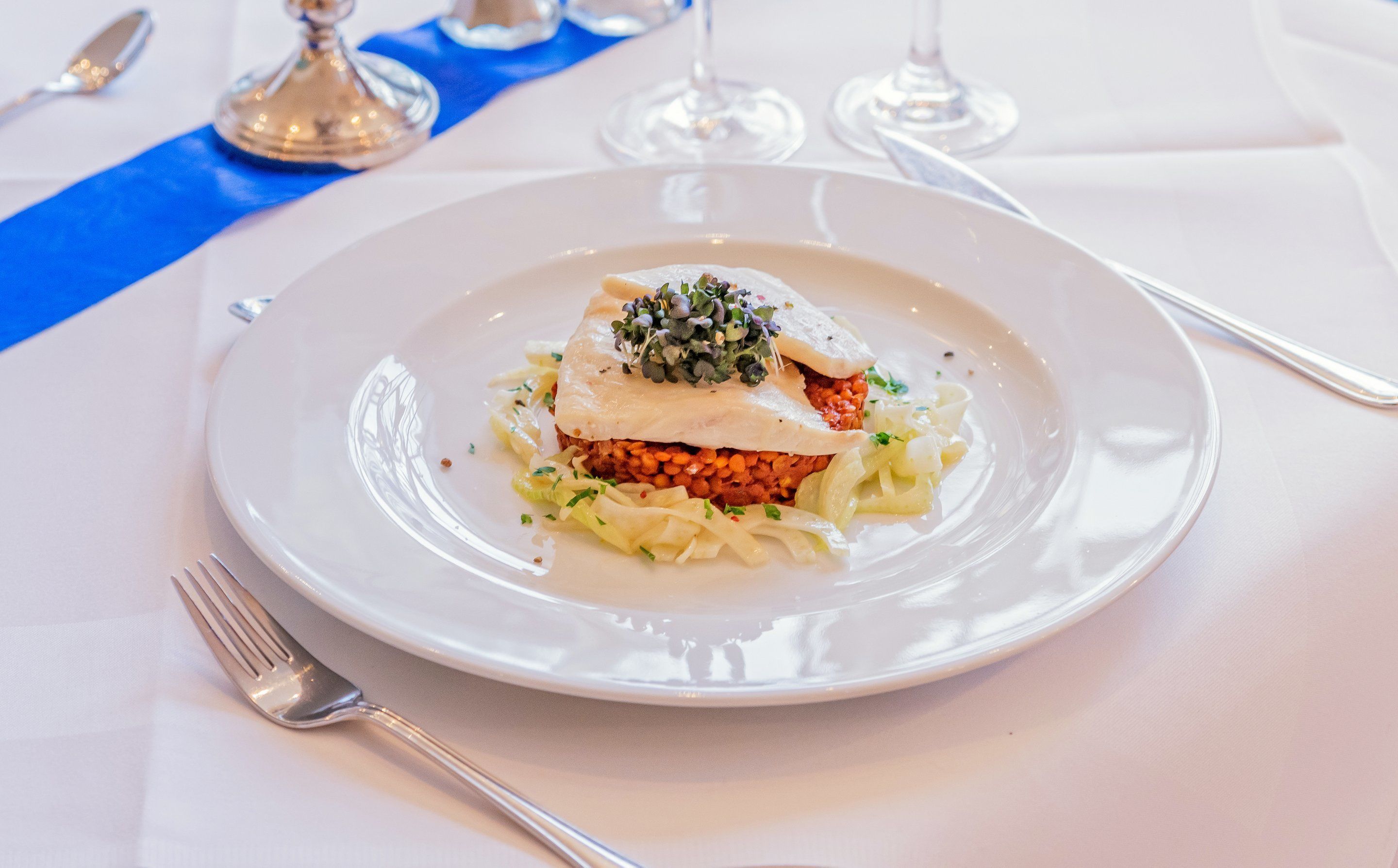 A plate of food with a white base, topped with a creamy sauce and a garnish of microgreens.