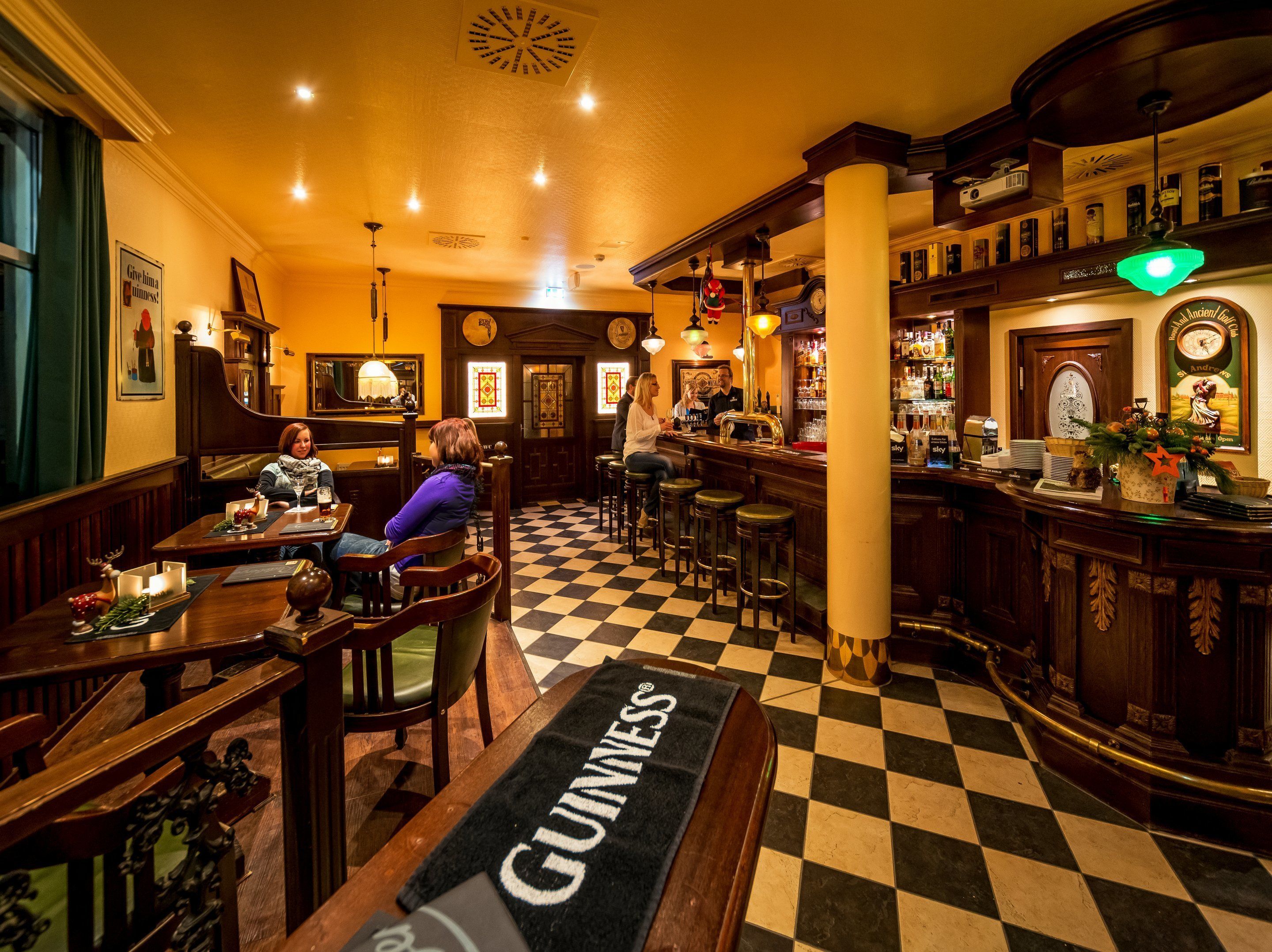 A bar area with a checkered floor, wooden furniture, and a Guinness-branded carpet.