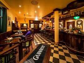 A bar area with a checkered floor, wooden furniture, and a Guinness-branded carpet.
