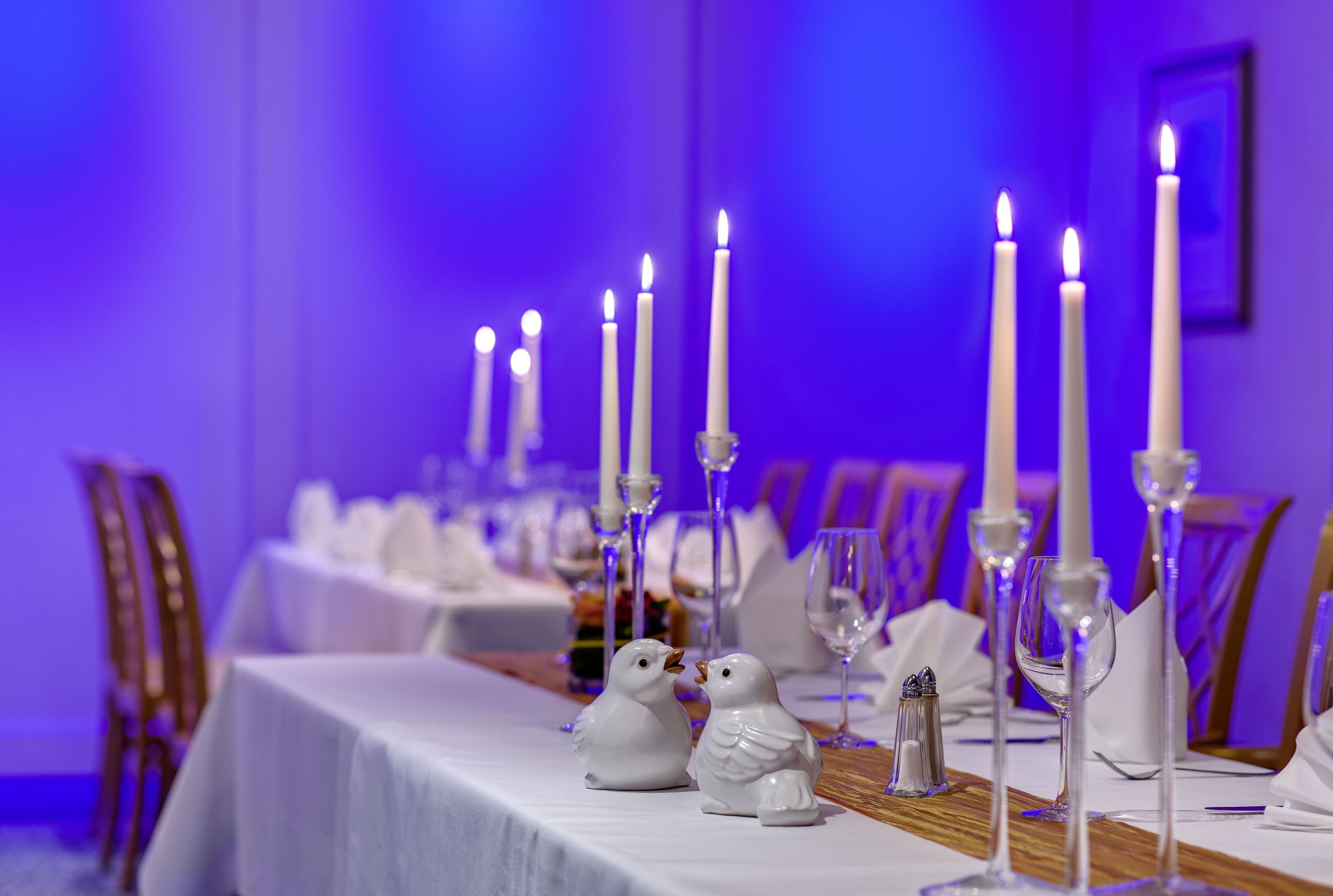 A dining table with white tablecloths, candles, and salt and pepper shakers.