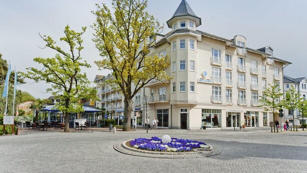 A hotel with a corner turret, outdoor seating, and a flower bed. - Aquamarin Hotel & Spa (Kuehlungsborn)