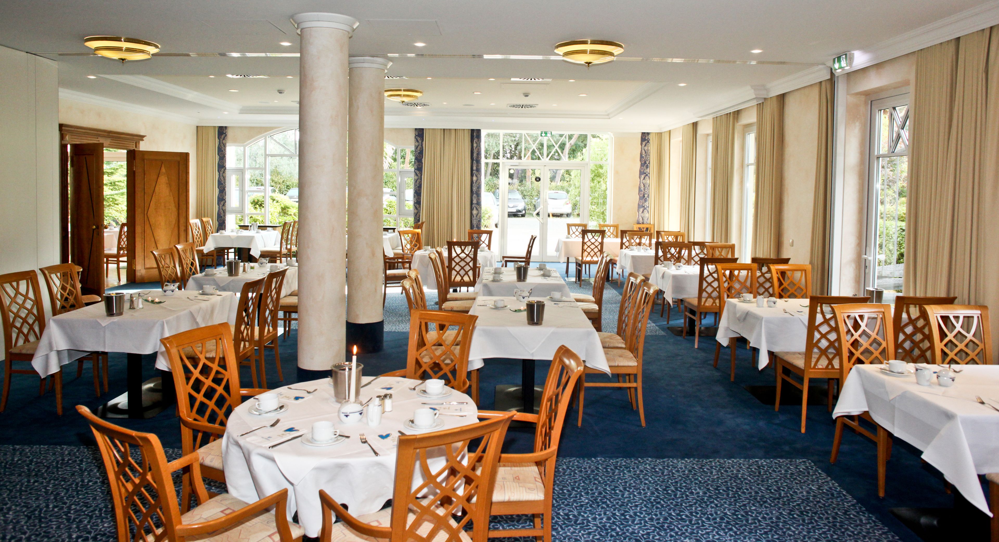 A spacious dining area with multiple tables and chairs, large windows, and a high ceiling.