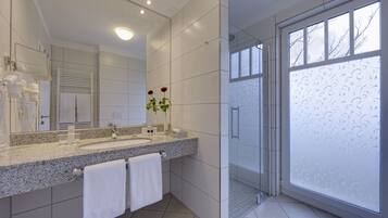 A modern bathroom with a granite countertop, a large mirror, two sinks, and a glass shower enclosure.