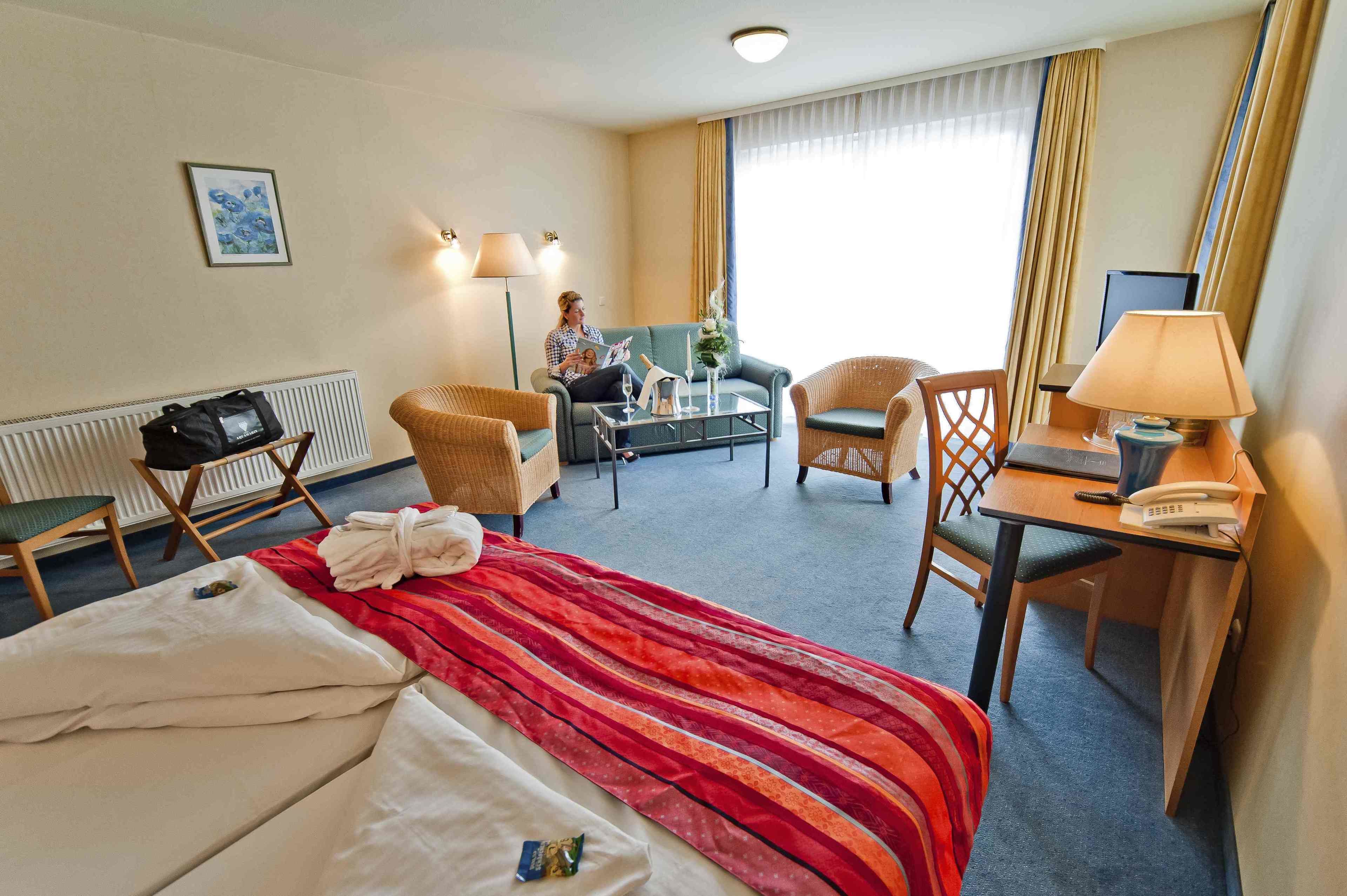 A hotel room with a bed, a desk, a chair, a sofa, and a window with curtains.