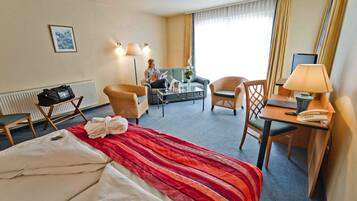 Ett hotellrum med en säng, ett skrivbord, en stol, en soffa och ett fönster med gardiner.