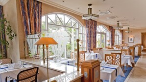A restaurant with tables set for dining, large windows with curtains, and a blue carpet. - Aquamarin Hotel & Spa (Kuehlungsborn)