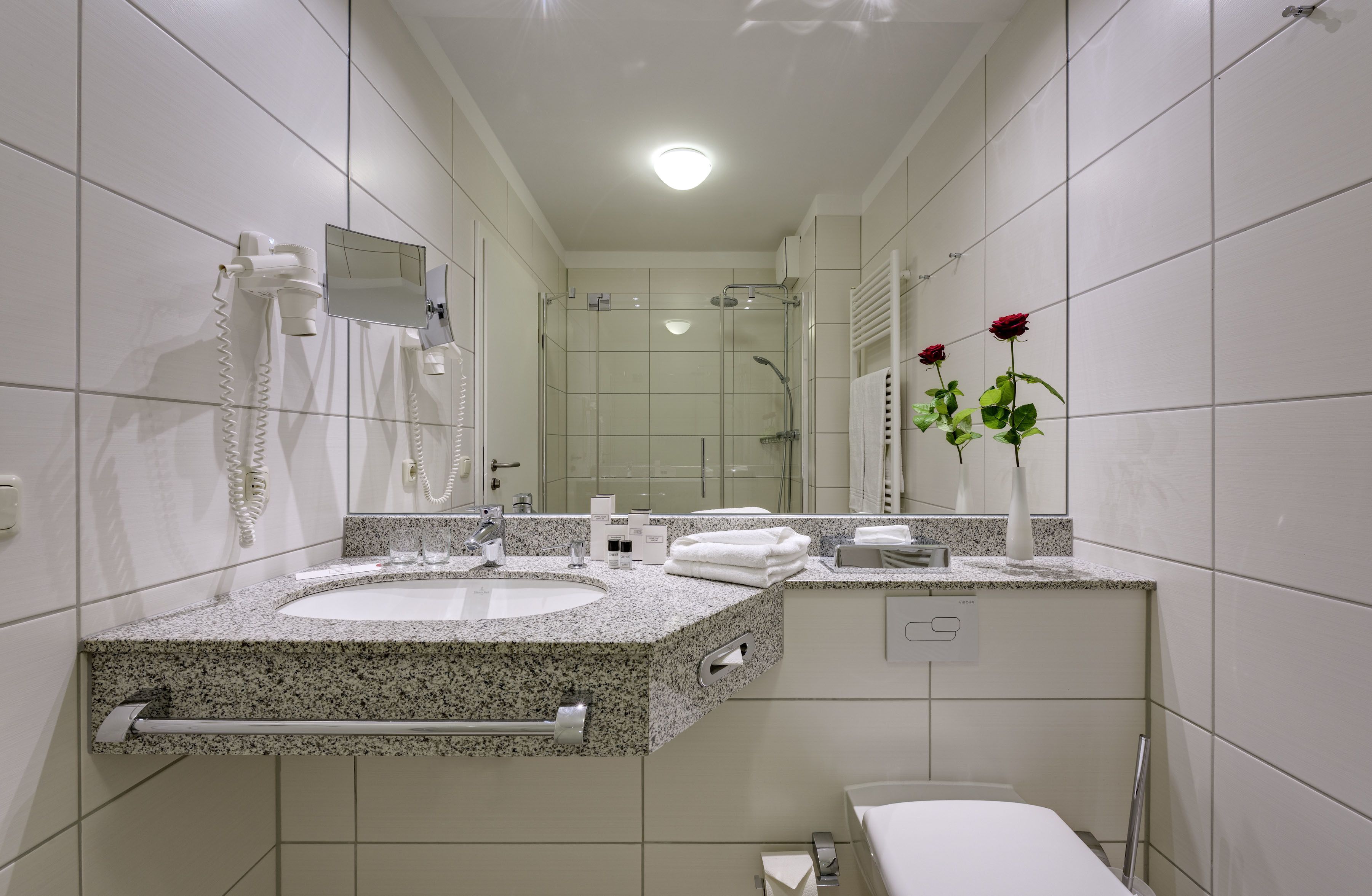 A modern bathroom with a granite countertop sink, a glass-enclosed shower, and a mirror above the sink.