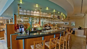 A bar area with a curved counter, multiple bar stools, and a variety of glassware and bottles. - Aquamarin Hotel & Spa (Kuehlungsborn)