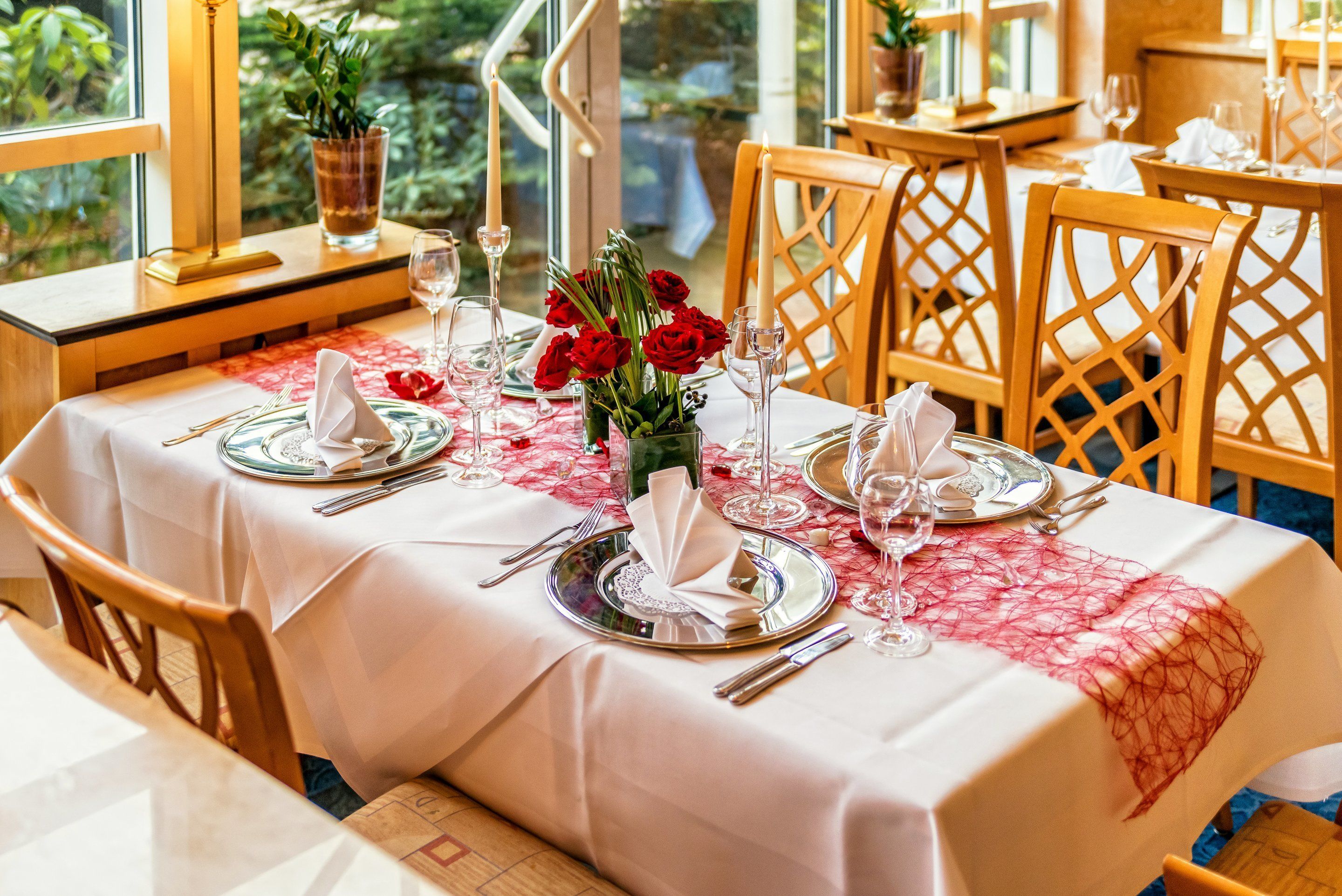 Ein Esstisch mit weißer Tischdecke, roten Rosen als Tischdekoration und Holzsesseln.