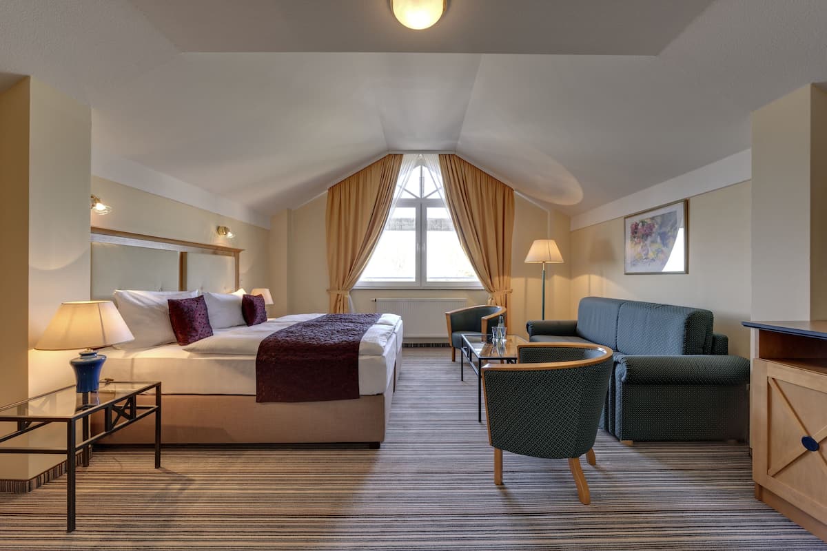 A hotel room with a bed, a desk, a chair, a sofa, and a window with curtains.