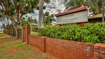 A sign for Bayside Holiday Apartments with a brick wall and greenery in the background.