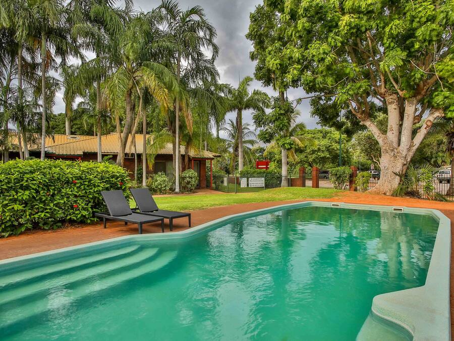 Ein Pool mit Liegestühlen, umgeben von üppiger Vegetation und einem kleinen Gebäude.