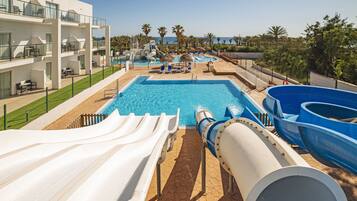 Un área de piscina con toboganes y sillas de descanso, piscina y un edificio con balcones.