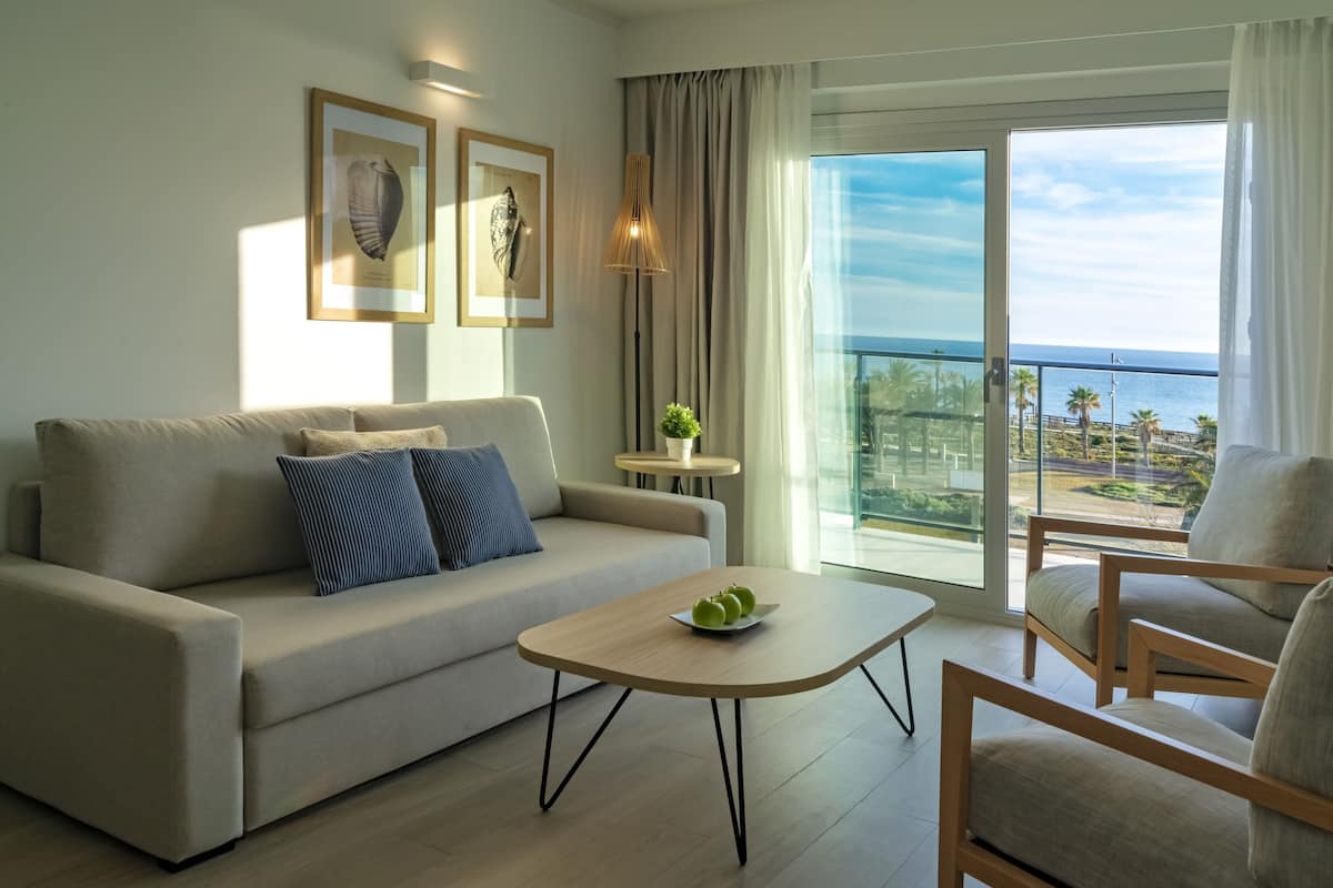 Ein modernes Wohnzimmer mit einer Couch, einem Couchtisch mit Äpfeln und Meerblick durch große Fenster.