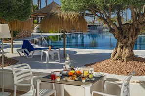 A poolside dining area with a table set for breakfast, overlooking a swimming pool. - Cabogata Jardín Hotel (Almeria)