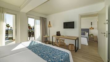 Habitación de hotel con una cama grande, un escritorio, una silla, un televisor y un balcón con vistas a palmeras.