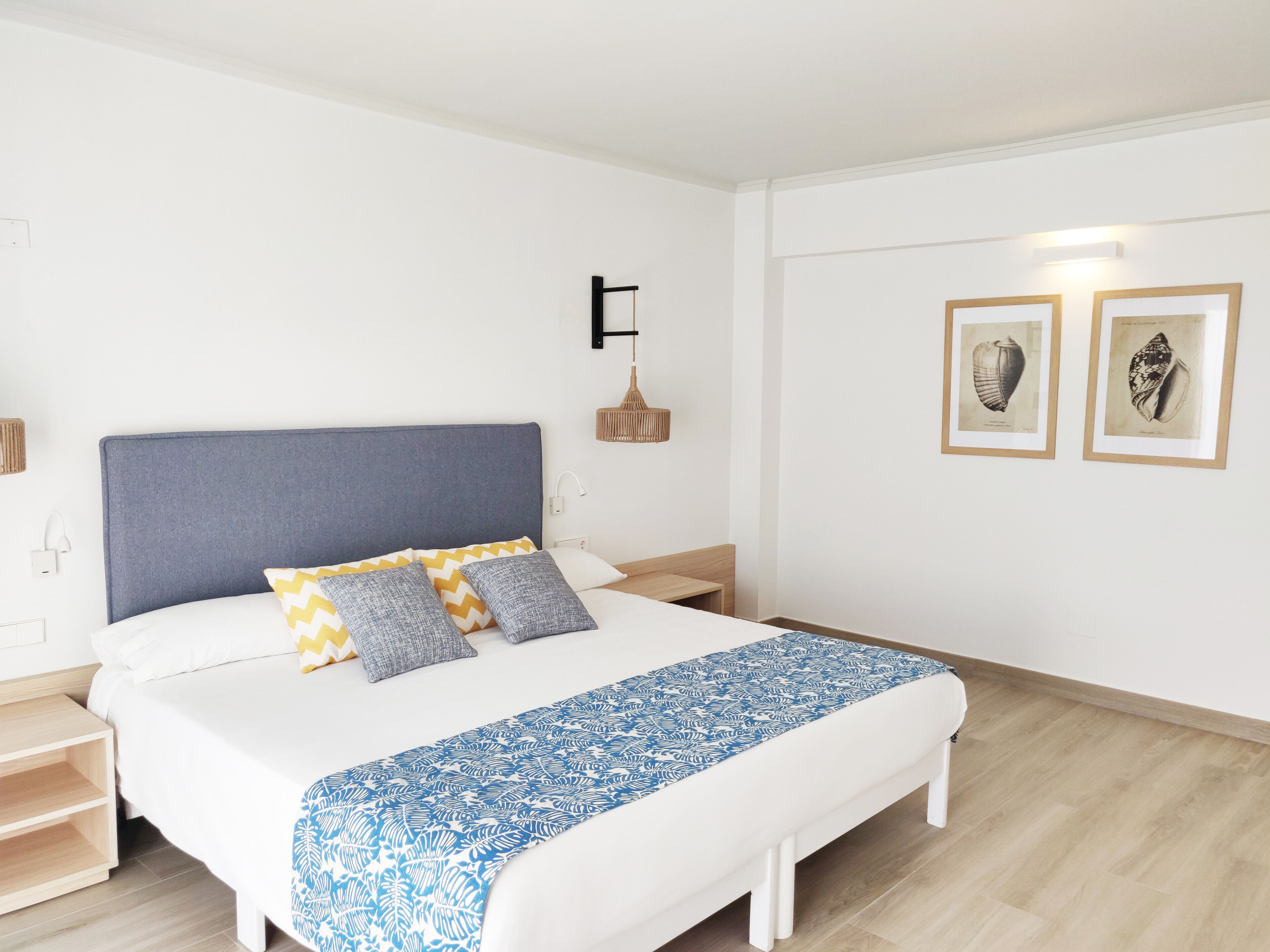 Ein ordentlich eingerichtetes Schlafzimmer mit einem Bett, Nachttischen, einer Wandlampe und gerahmten Bildern.