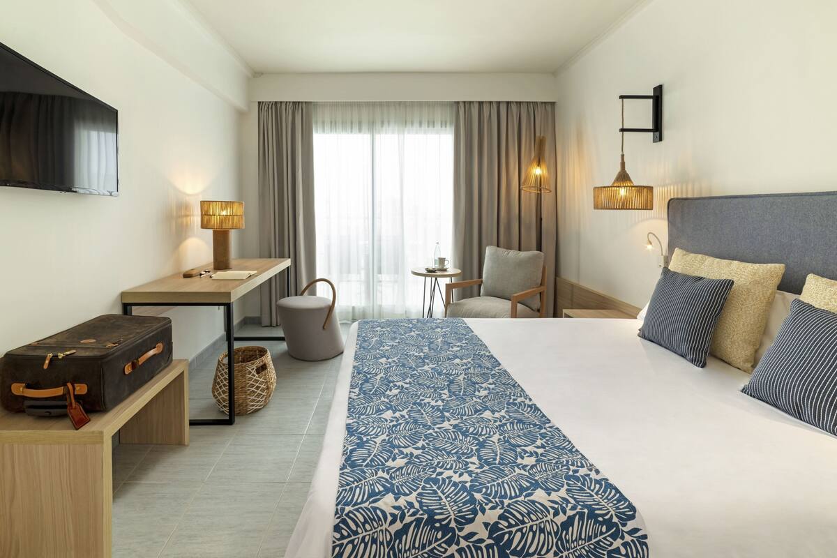 Ein Hotelzimmer mit einem Bett, einem Schreibtisch, einem Stuhl, einem Fernseher und einer Lampe.