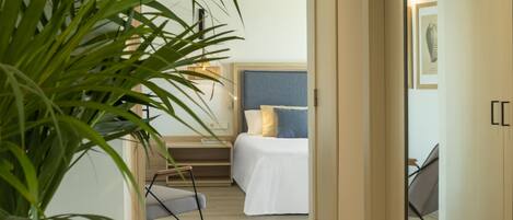 A bedroom with a bed, bedside table, lamp, and a potted plant.