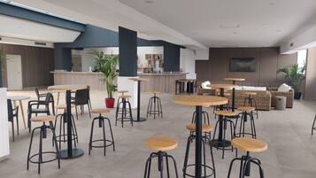 Un café moderno con mesas y taburetes redondos, una zona de bar y plantas en macetas.