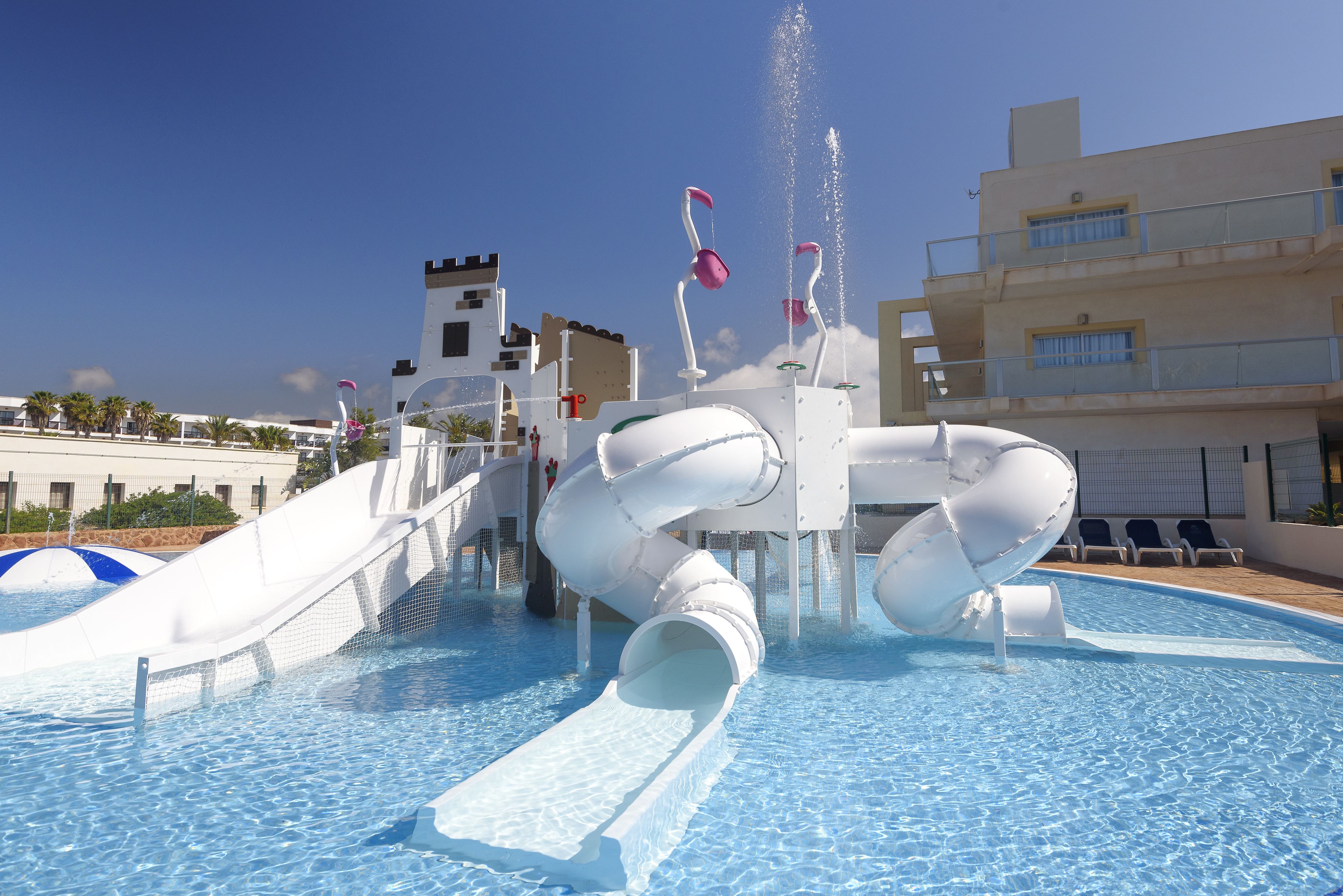 Een waterpark met een groot zwembad, glijbanen en een kasteelachtige constructie op de achtergrond.