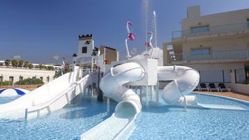 Een waterpark met een groot zwembad, glijbanen en een kasteelachtige constructie op de achtergrond.