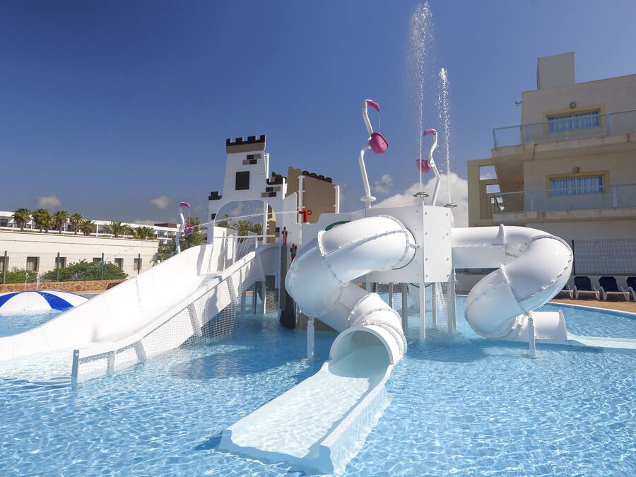 Een waterpark met een groot zwembad, glijbanen en een kasteelachtige constructie op de achtergrond.