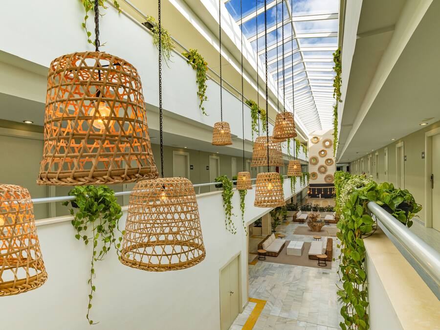 Amplio espacio interior con lámparas de mimbre colgantes, un techo alto y vistas a un nivel inferior a través de un pasillo de cristal.