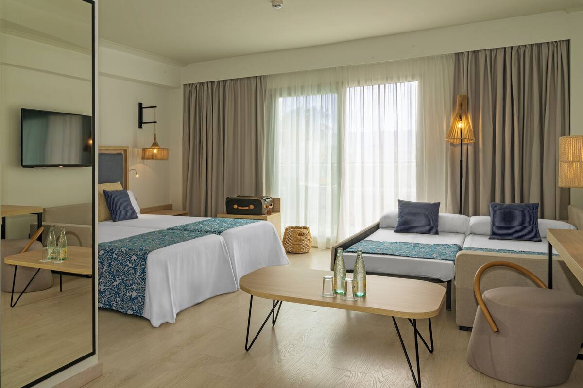Ein modernes Hotelzimmer mit zwei Betten, einem Sofa, einem Esstisch und einem Fernseher.