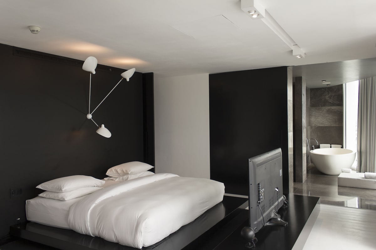 A modern bedroom with a large bed, a flat-screen TV, and a built-in bathtub.