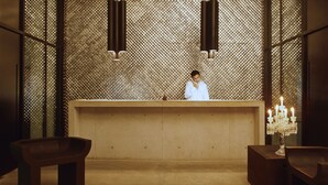 Un espace d’accueil avec un mur orné de motifs, une réceptionniste, un chandelier et un tapis en fourrure.