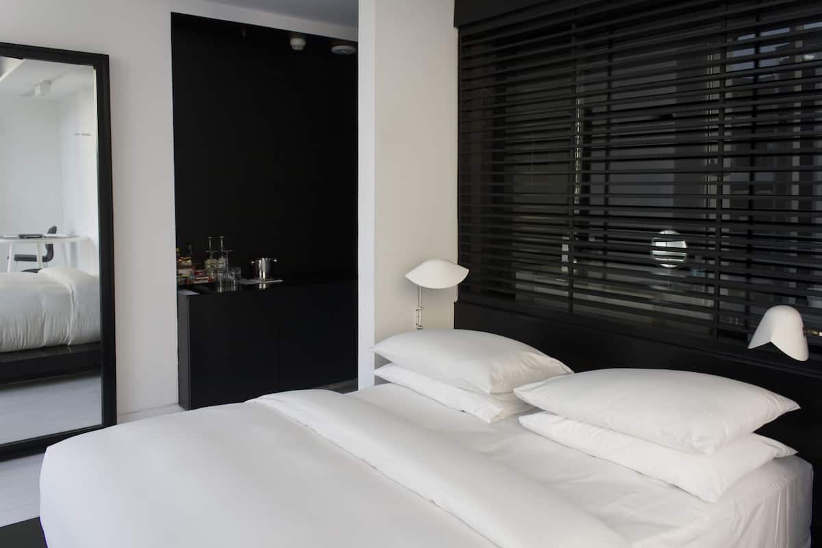 A modern bedroom with a large bed, a mirror, a nightstand, and a window with blinds.