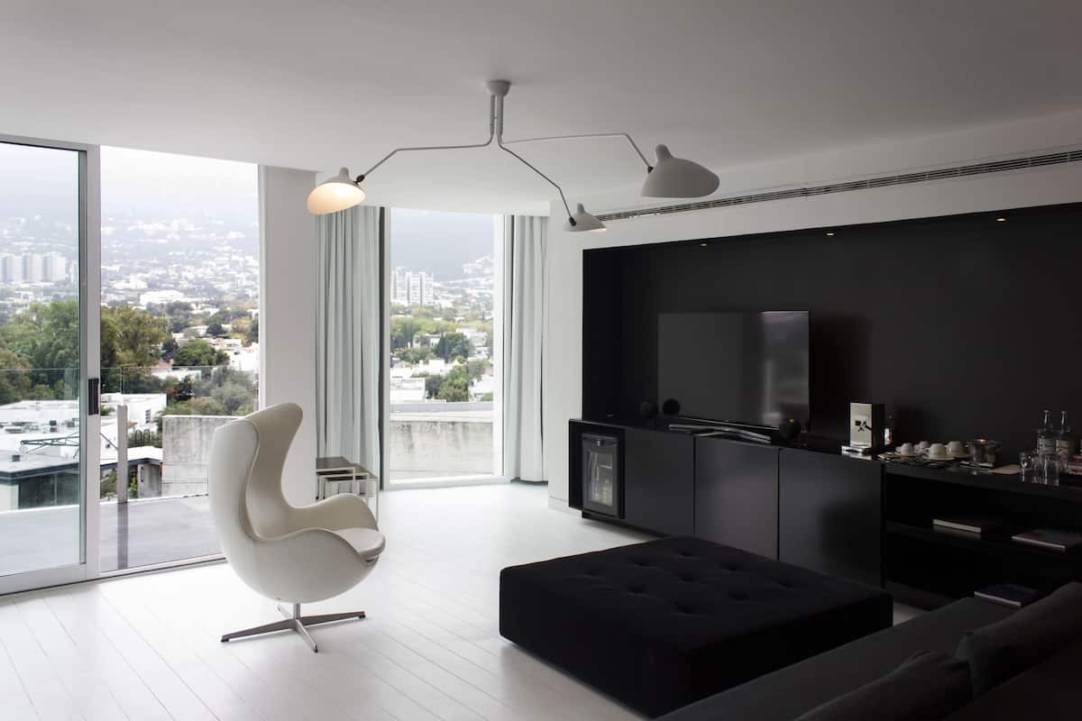 A modern living room with a large window, a white chair, a black ottoman, and a black sofa.