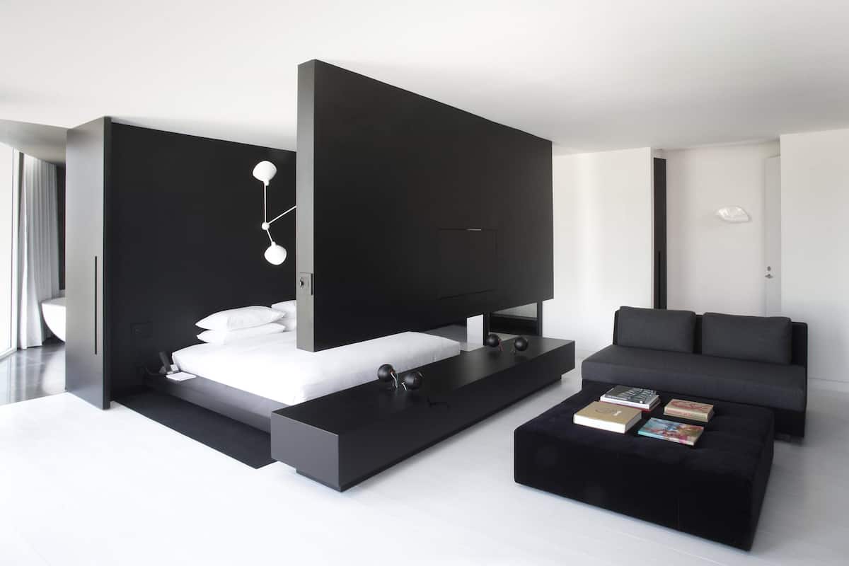A modern bedroom with a bed, bedside tables, a black sofa, and a coffee table with books.