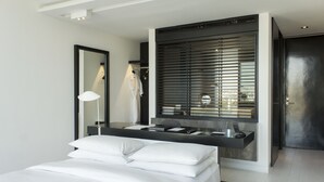 Une chambre moderne avec un grand lit, une table de chevet, un miroir et une fenêtre avec des stores.