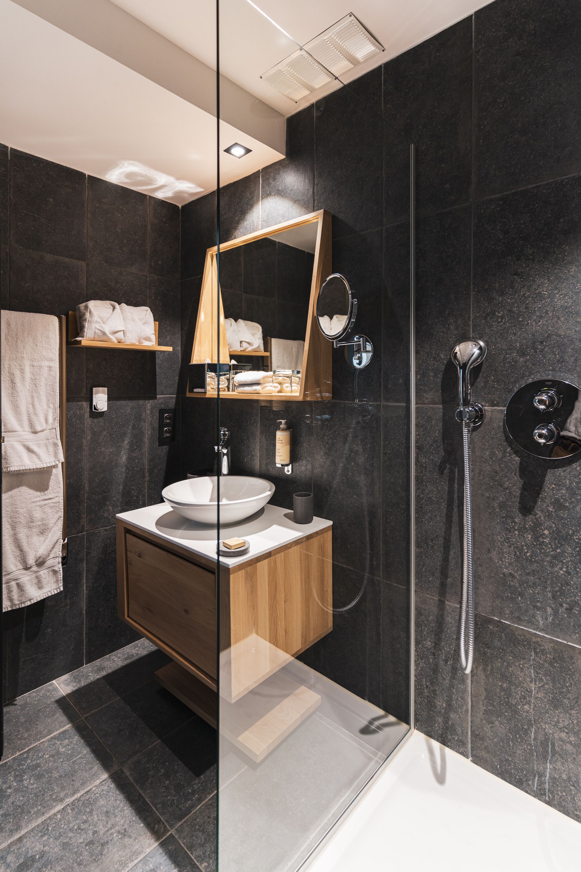A modern bathroom with a glass shower enclosure, a wooden vanity, a large mirror, and a white bathtub.