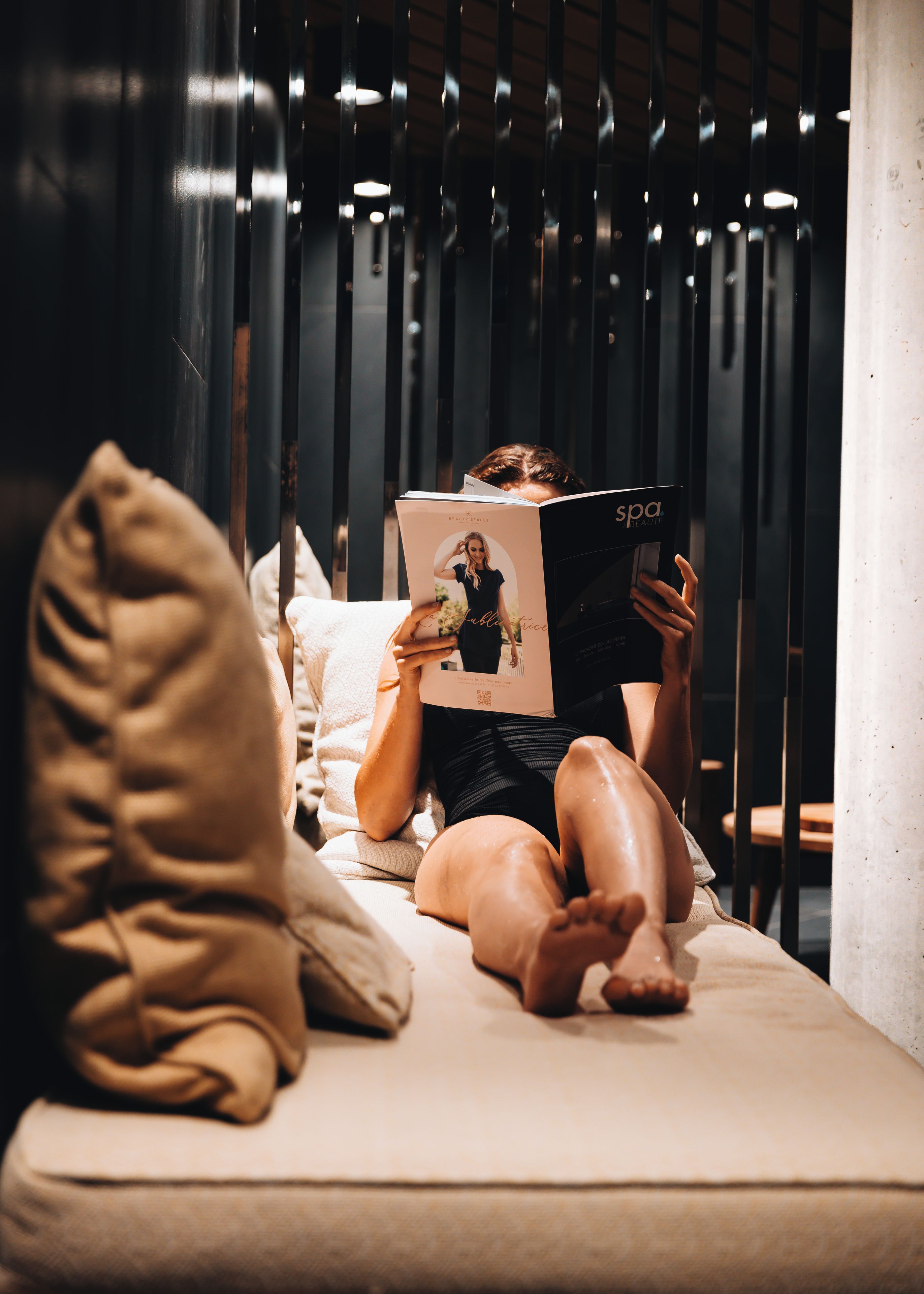 A person lying on a bed reading a book in a room with a modern design, featuring a striped wall and a visible column.