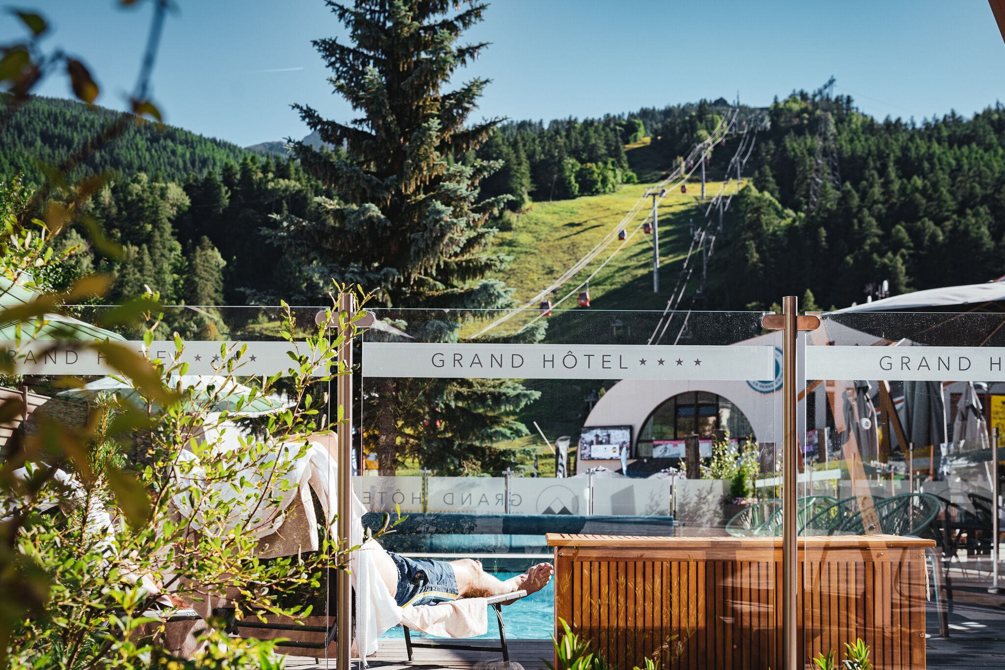 Ett poolområde med en solstol och ett trädäck, omgivet av grönska.