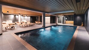 A modern indoor swimming pool with wooden loungers and a stone-tiled floor. - Grand Hôtel & Spa NUXE Serre Chevalier (Saint-Chaffrey)