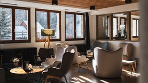 A modern living room with large windows, a round coffee table, and several upholstered chairs. - Grand Hôtel & Spa NUXE Serre Chevalier (Saint-Chaffrey)