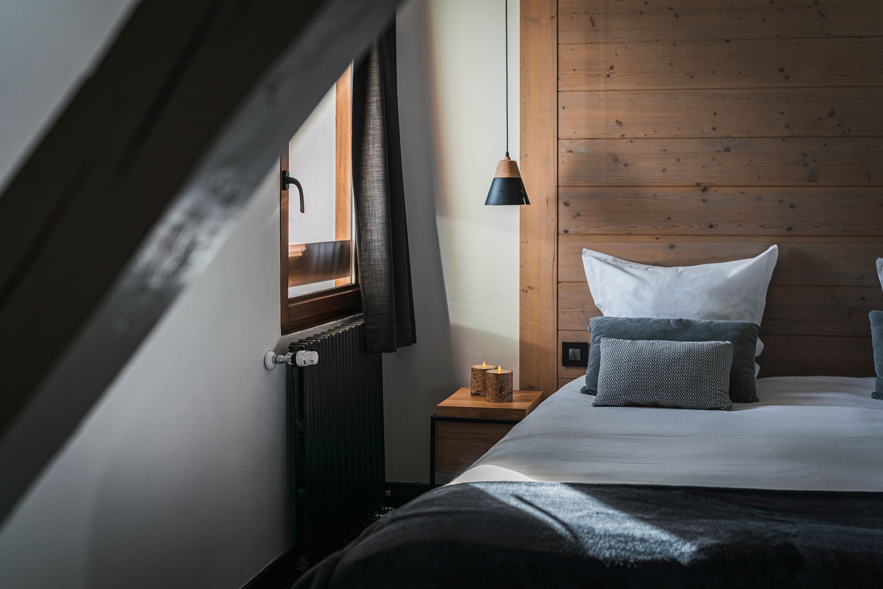 Un dormitorio con cabecera de madera, una mesita de noche con lámpara y una ventana con cortinas.