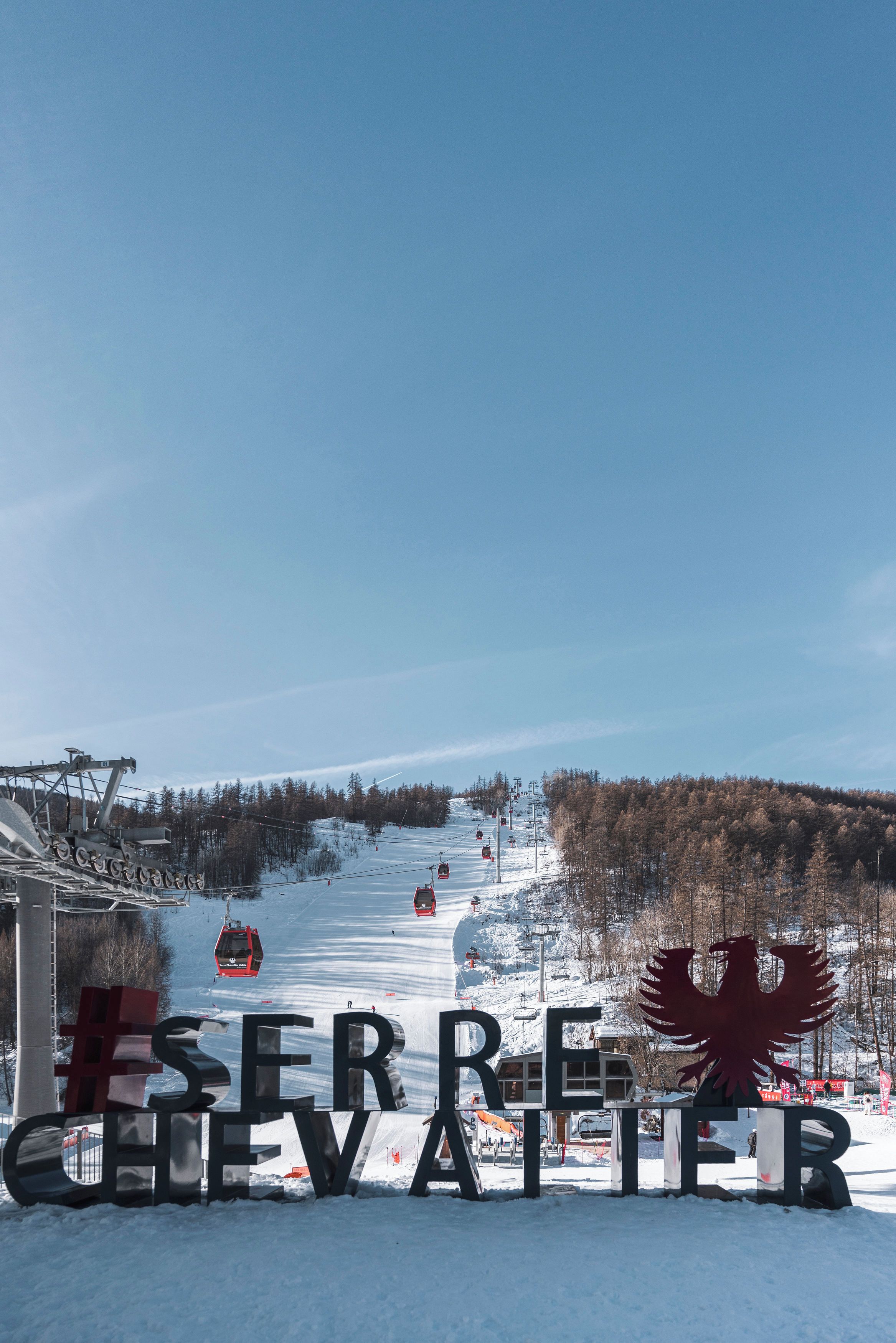 A ski resort entrance with a large sign reading 'ESERE CHEVATOIR' and a red eagle emblem.