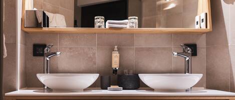 A modern bathroom with two sinks, a large mirror, and wooden cabinetry.