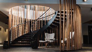 A spiral staircase with a wooden finish and metal railings, leading to a seating area with a modern chair and a small table. - Grand Hôtel & Spa NUXE Serre Chevalier (Saint-Chaffrey)