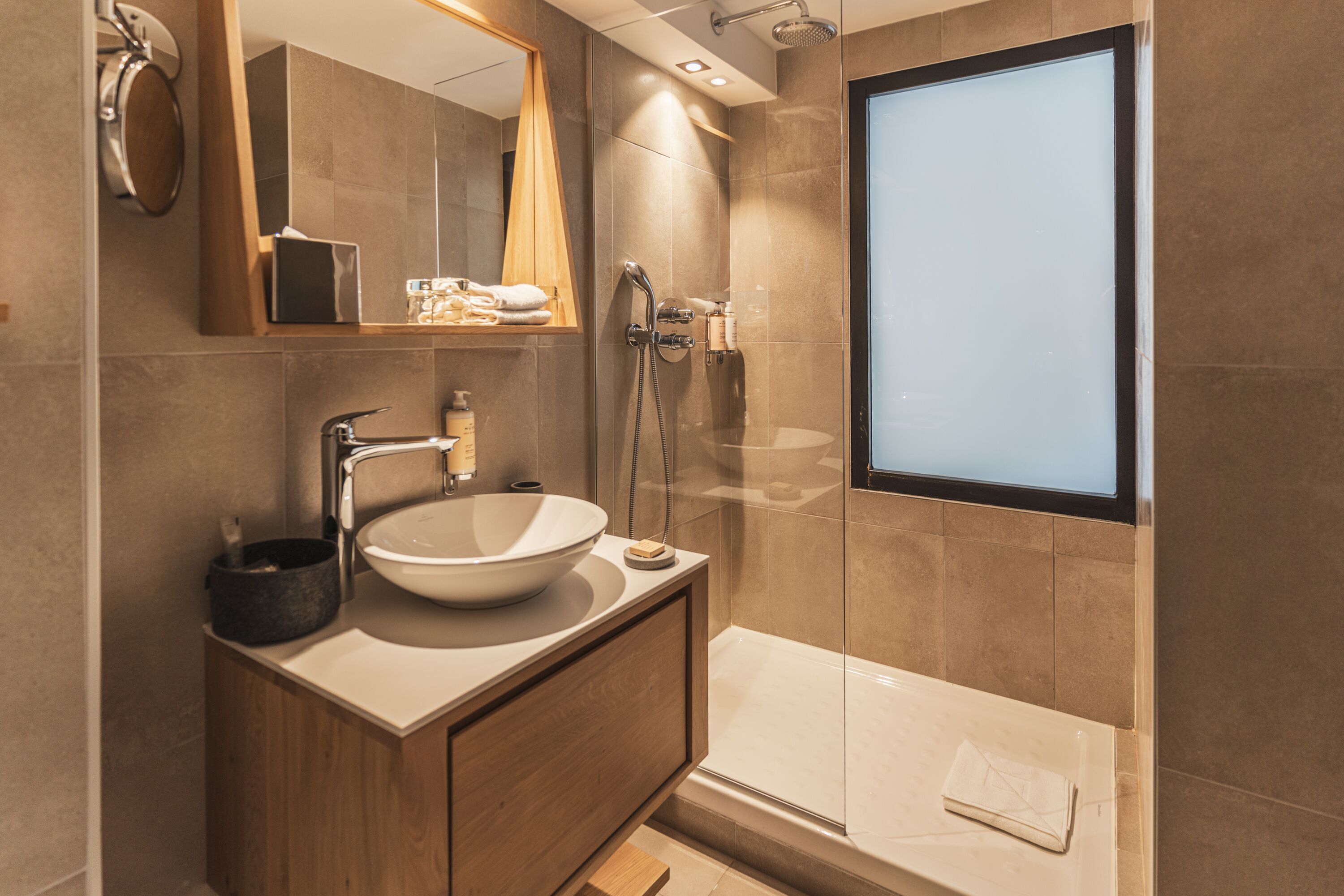 A modern bathroom with a large mirror, a vessel sink, a handheld showerhead, and a glass-enclosed bathtub.