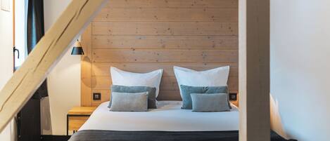A bedroom with a sloped ceiling, a bed with white linens and patterned pillows, a nightstand with a lamp, and a wooden headboard.