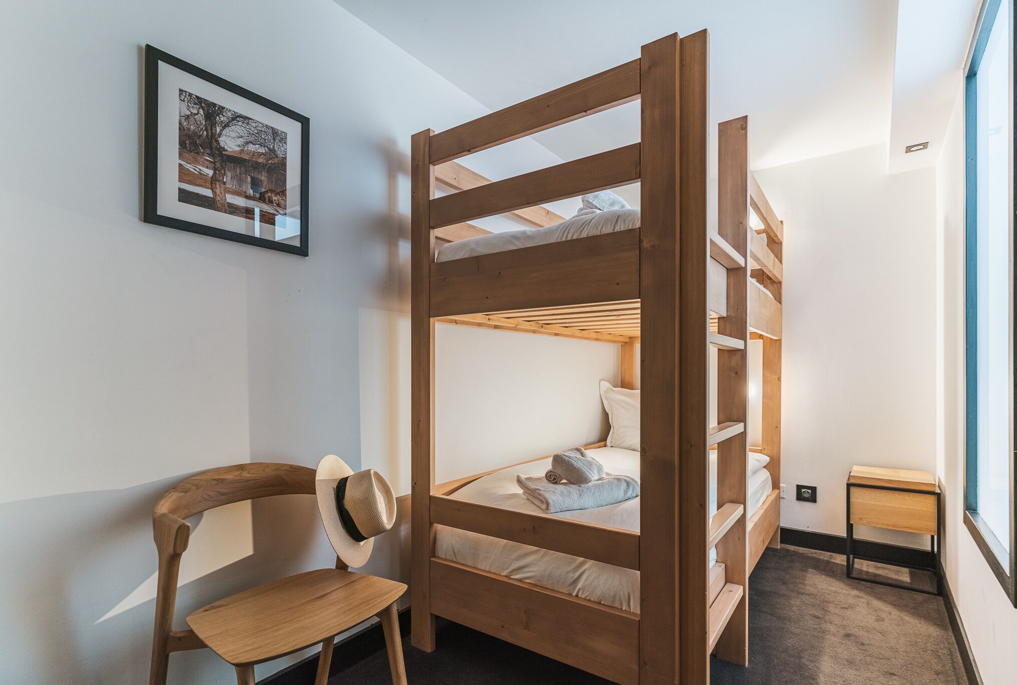 A bunk bed room with a wooden headboard, a chair, a small table, and a framed picture on the wall.