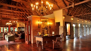 A spacious lobby with a high wooden ceiling, a large chandelier, and stone pillars. - Imbali Safari Lodge (Imbali Concession)